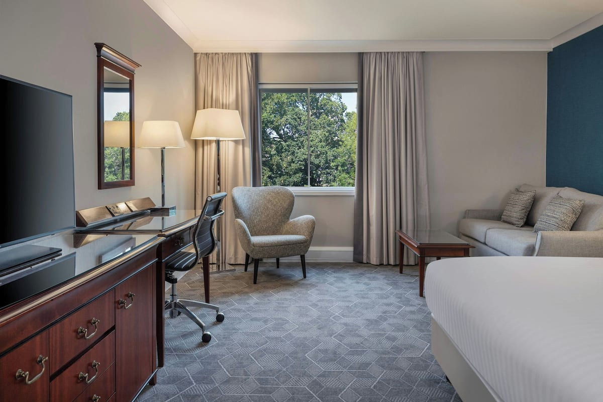 Une chambre d’hôtel comprenant un lit, un bureau avec une chaise, une télévision et une fenêtre avec des rideaux.