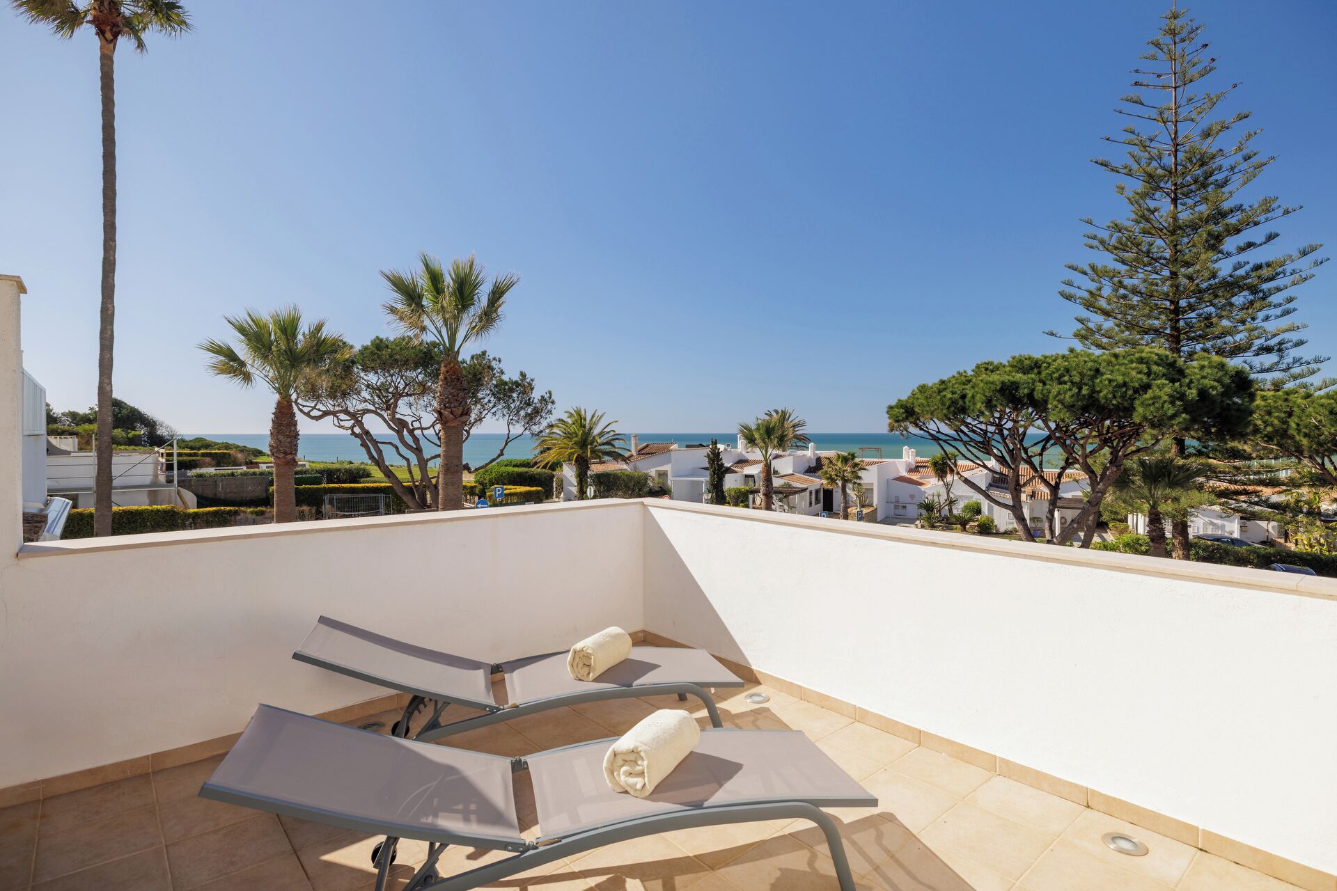 A rooftop terrace with two lounge chairs, a view of the sea, and surrounding buildings.