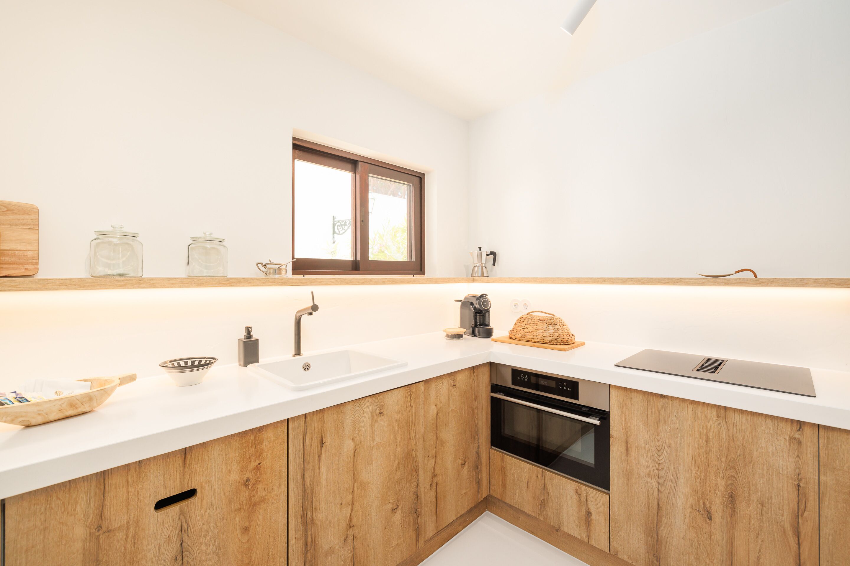 A modern kitchen with wooden cabinets, a white countertop, a built-in oven, and a window above the sink.