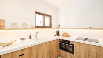 A modern kitchen with wooden cabinets, a white countertop, a built-in oven, and a window above the sink.