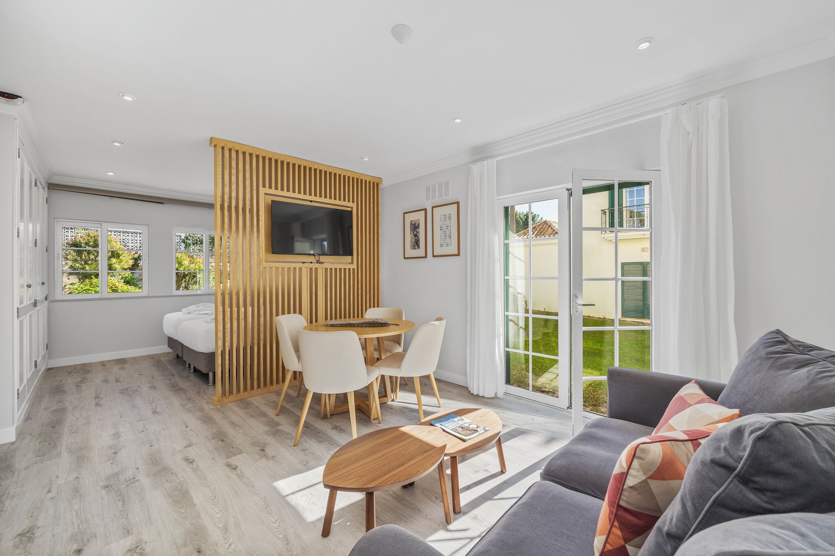 Una sala moderna con un sofá, una mesa de centro, un televisor, un comedor con sillas y un ventanal corredizo al exterior.
