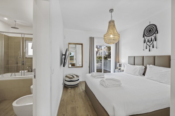 Una habitación de hotel moderna con una cama grande, ducha, tocador y vistas al exterior.