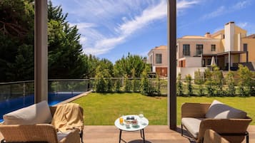 Un patio al aire libre con muebles de mimbre, una mesita con bebidas y aperitivos, y vistas a una piscina y edificios residenciales.