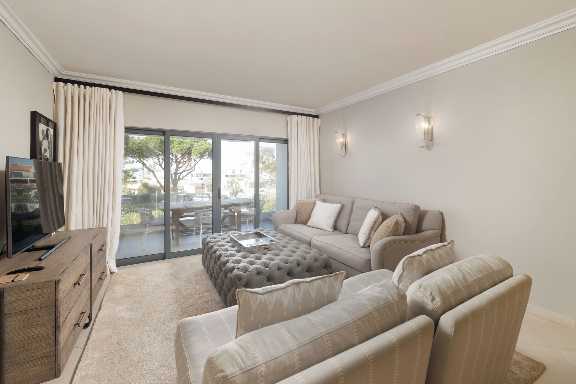 A living room with a sofa, ottoman, TV, and a sliding glass door leading to an outdoor area.