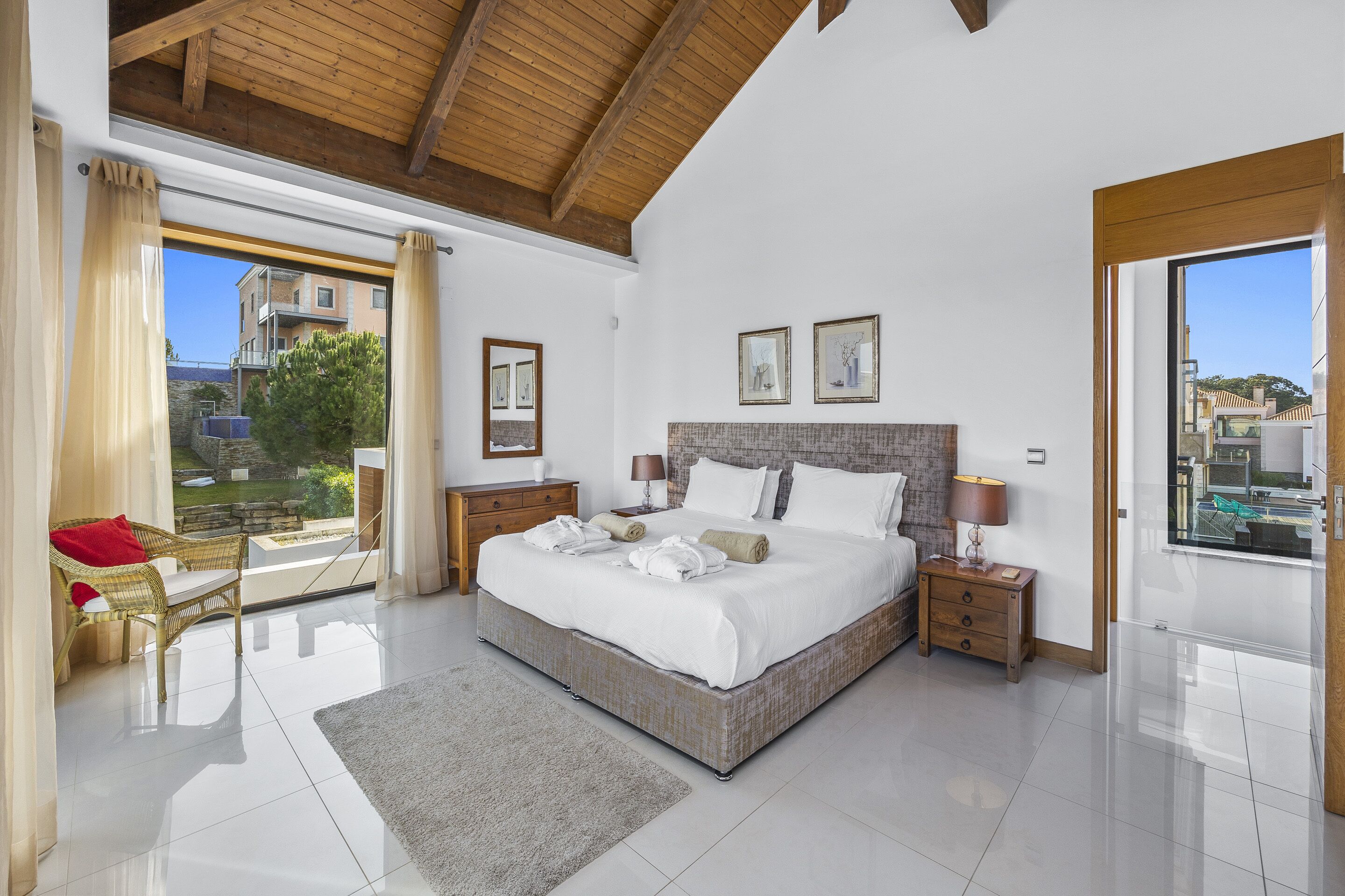 Un dormitorio amplio con una cama grande, vigas de madera en el techo, un balcón con vistas y una habitación bien iluminada con luz natural.