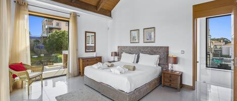 Quarto espaçoso com cama grande, vigas de madeira no teto, varanda com vista e ambiente bem iluminado pela luz natural.