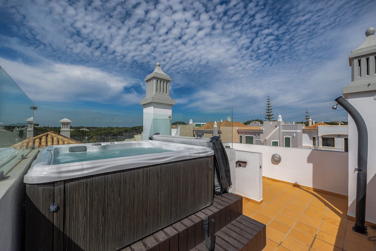 A rooftop with a hot tub, a view of the cityscape, and a clear sky.