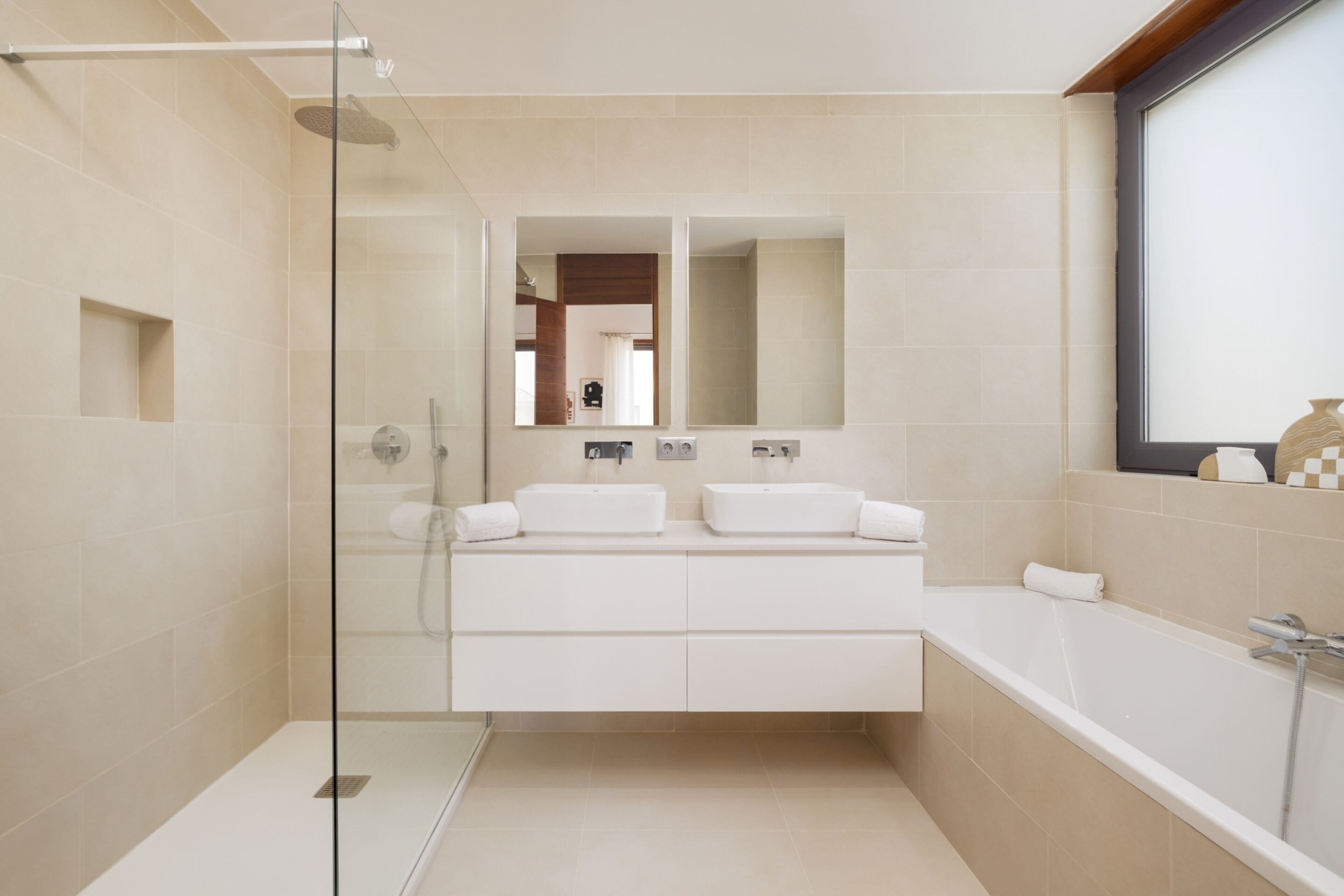 A modern bathroom with a glass shower enclosure, a large bathtub, and a vanity with two sinks.