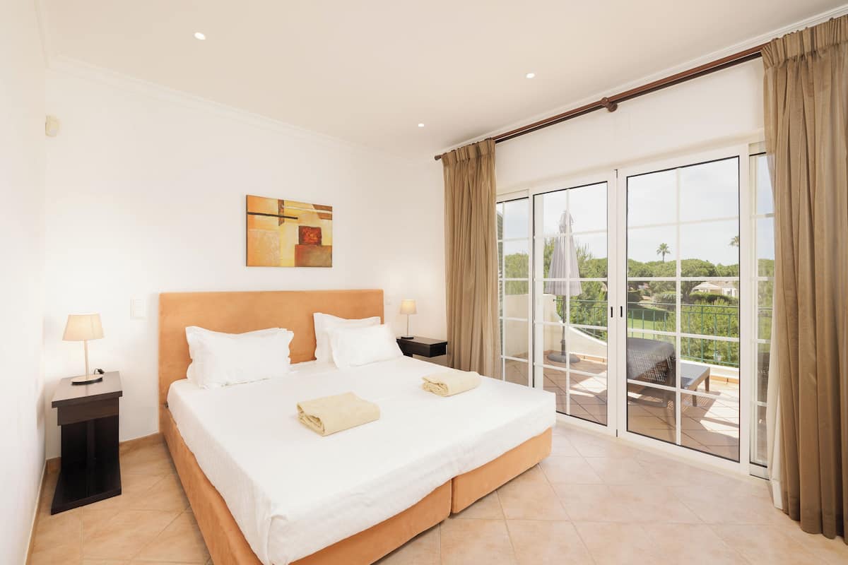 A hotel room with a large bed, a nightstand, a painting on the wall, and a sliding glass door to an outdoor area.