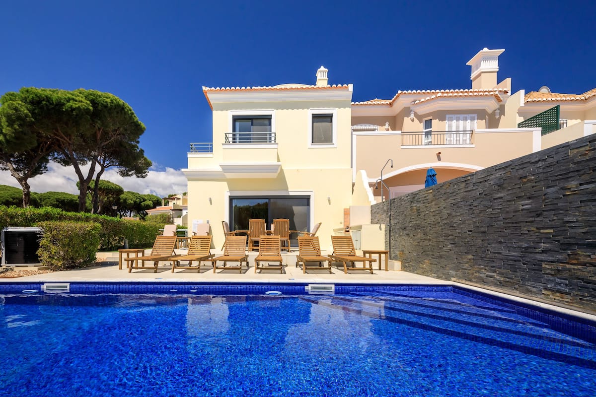 A modern villa with a swimming pool, outdoor seating, and a stone wall.