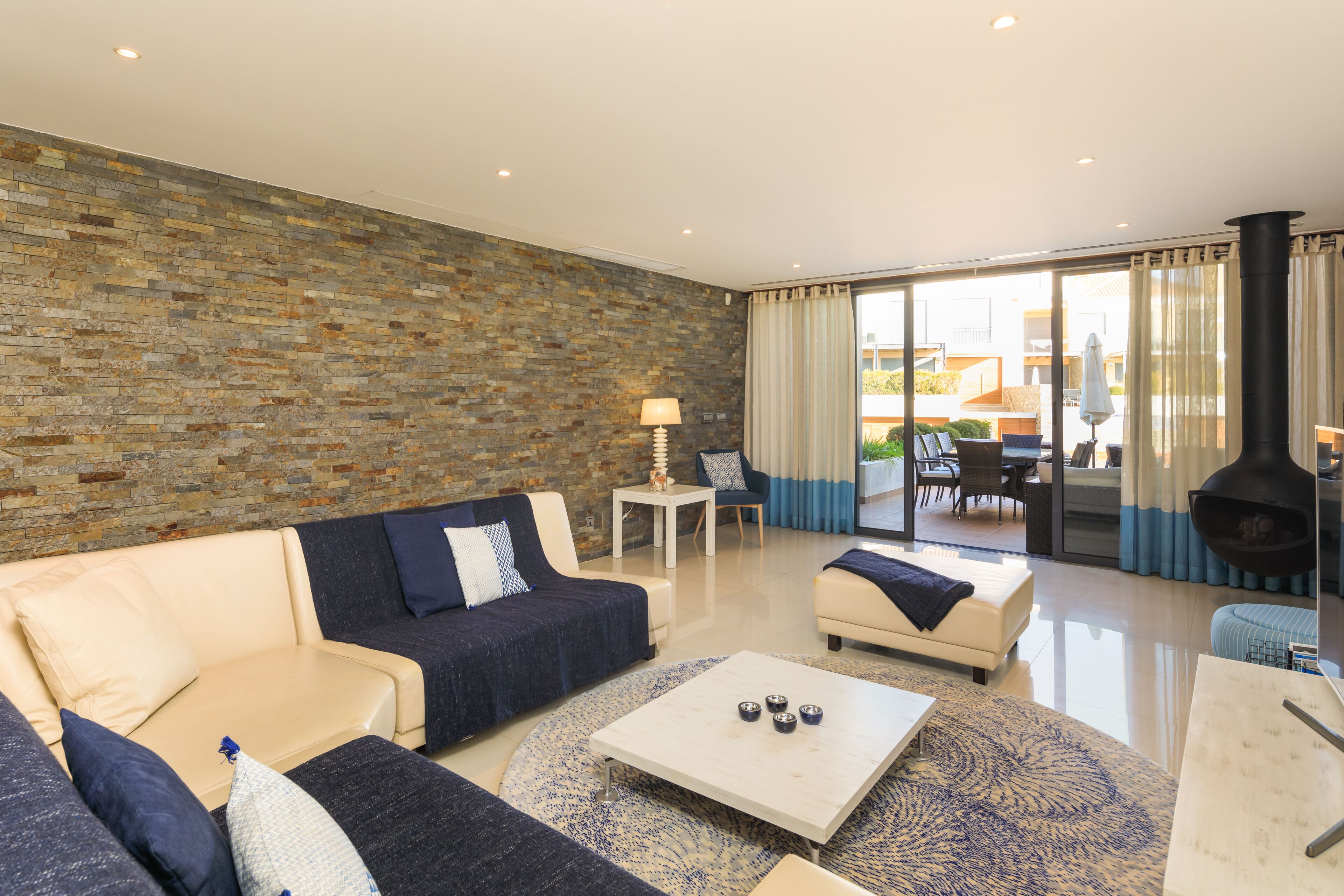 A modern living room with a stone wall, a sofa set, a coffee table, and a view of the outdoor patio.