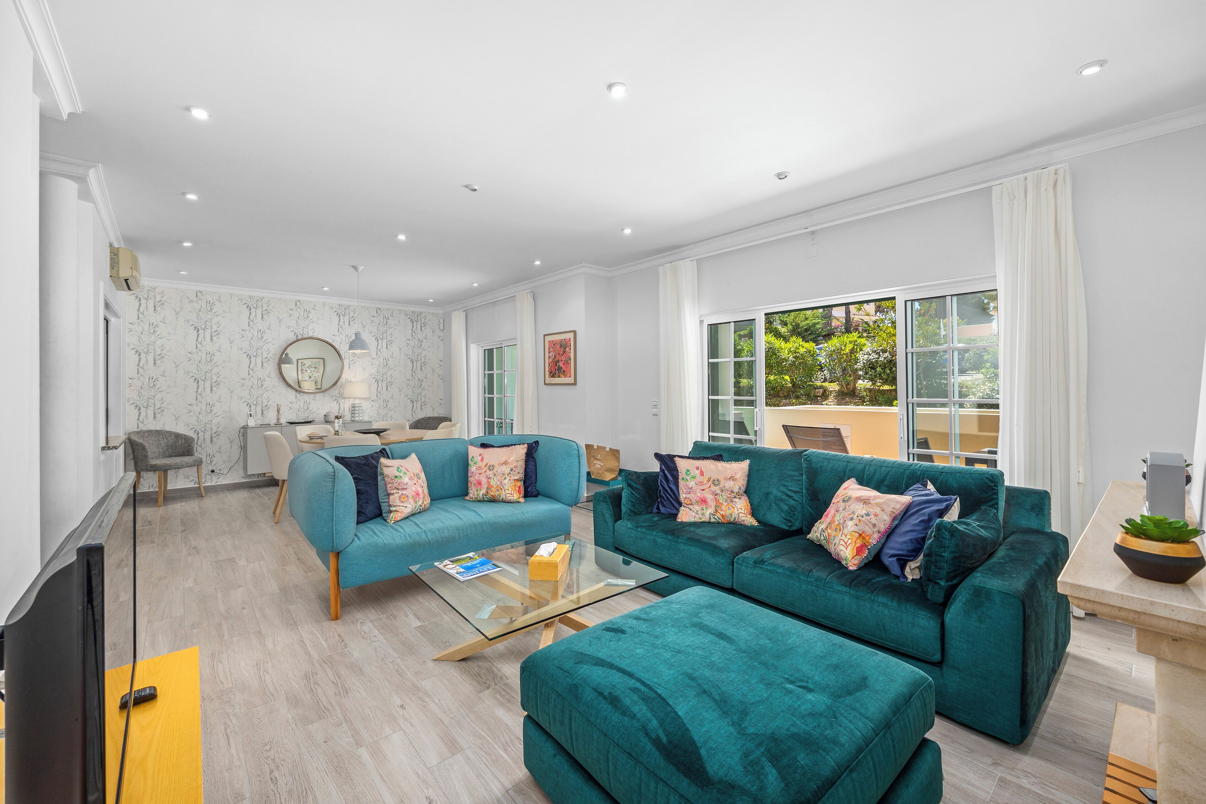 A modern living room with teal sofas, a glass coffee table, and a flat-screen TV.