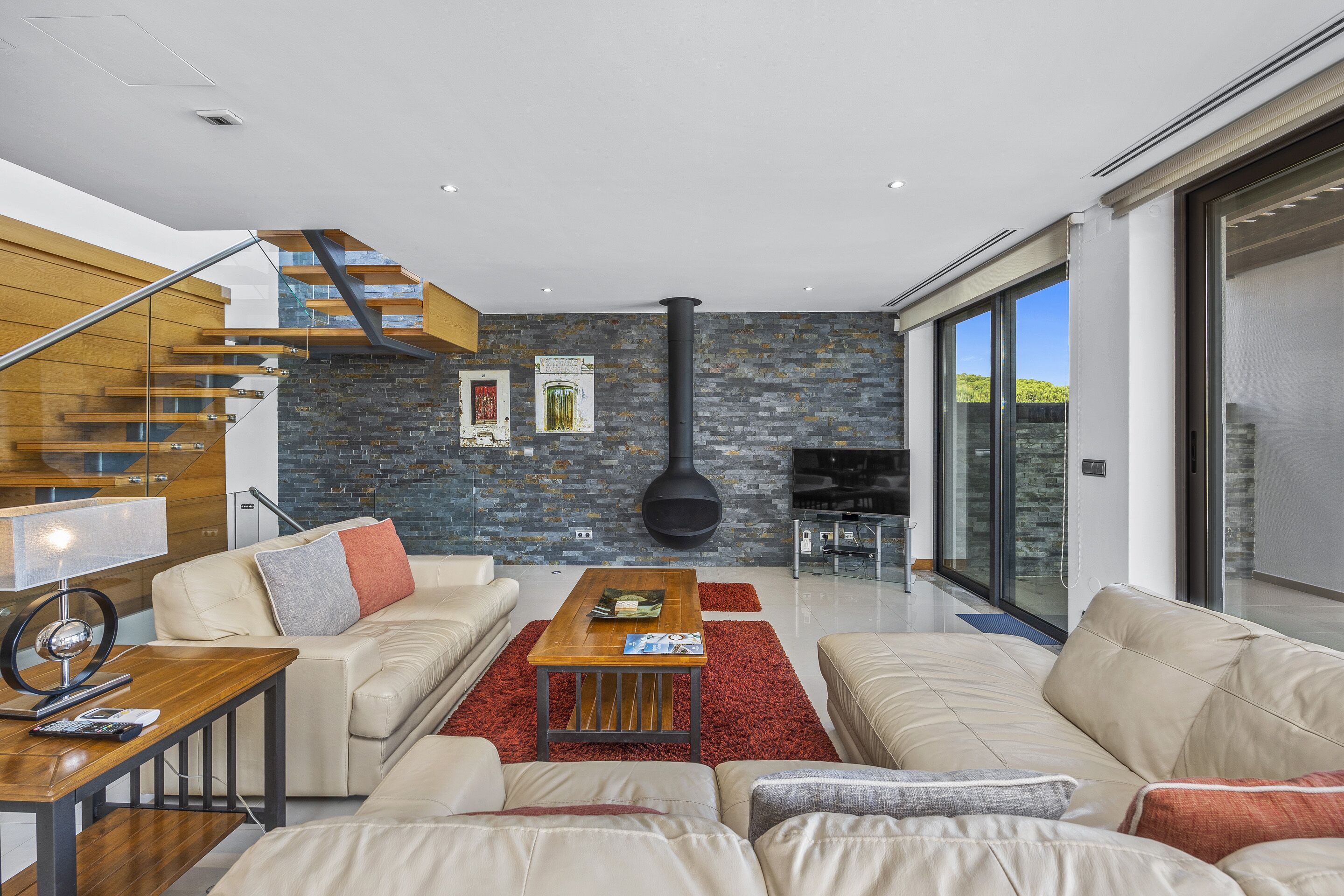 A modern living room with a staircase, a fireplace, and a large window.