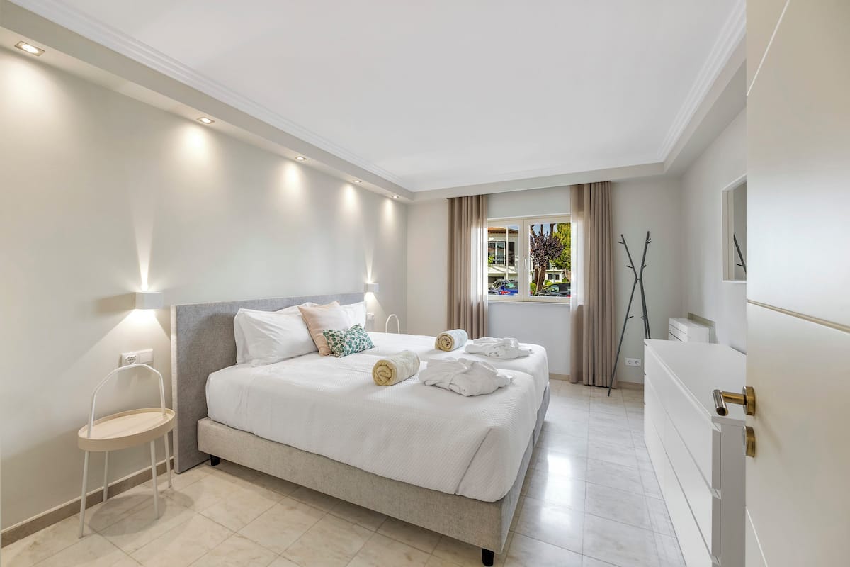A modern hotel room with a large bed, bedside tables, a desk, and a window with curtains.