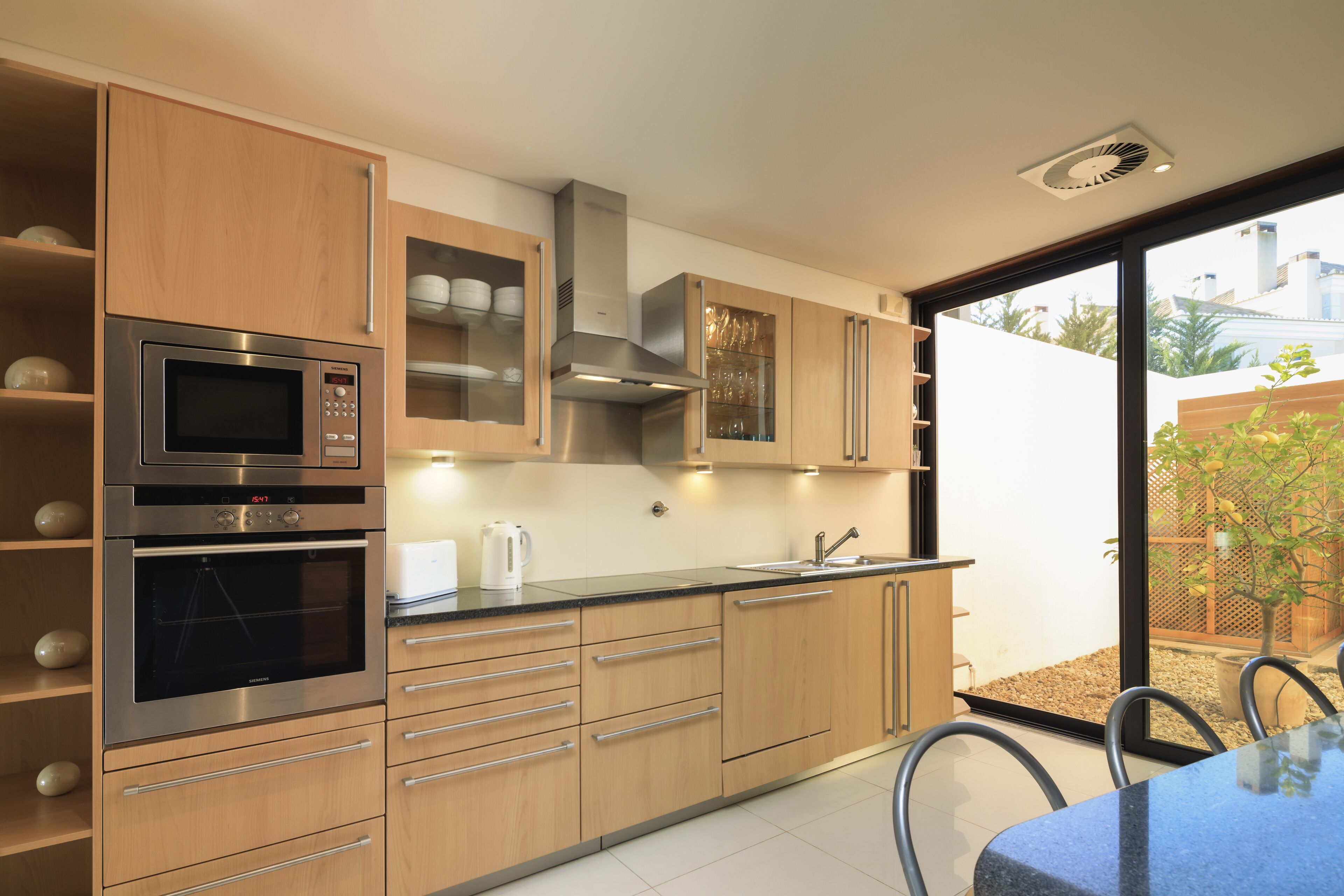 A modern kitchen with stainless steel appliances, wooden cabinets, and a large window offering a view of the outdoors.