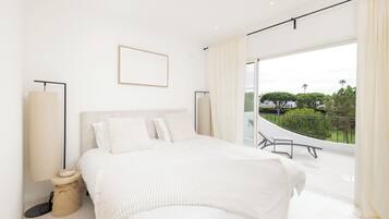 Un dormitorio moderno con una cama grande, una mesita de noche, una lámpara y vistas al exterior.