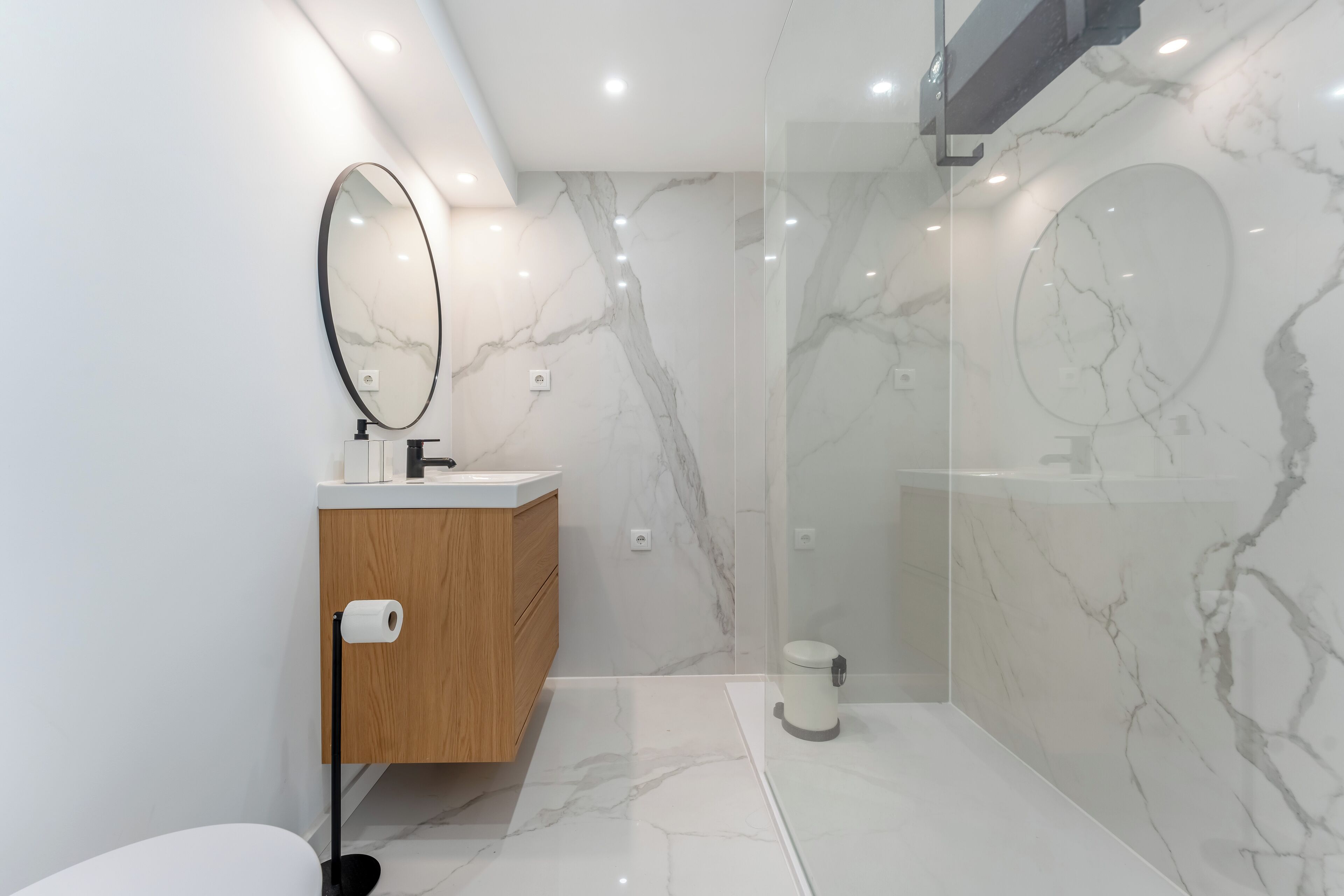 Un baño moderno con ducha de mármol, tocador de madera y un espejo grande.