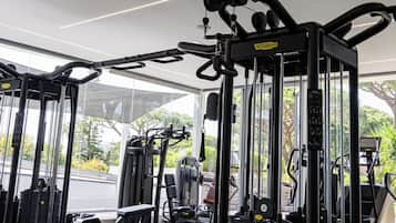 Un gimnasio con diversas máquinas de ejercicio, bancos y una zona cubierta con ventanas amplias.