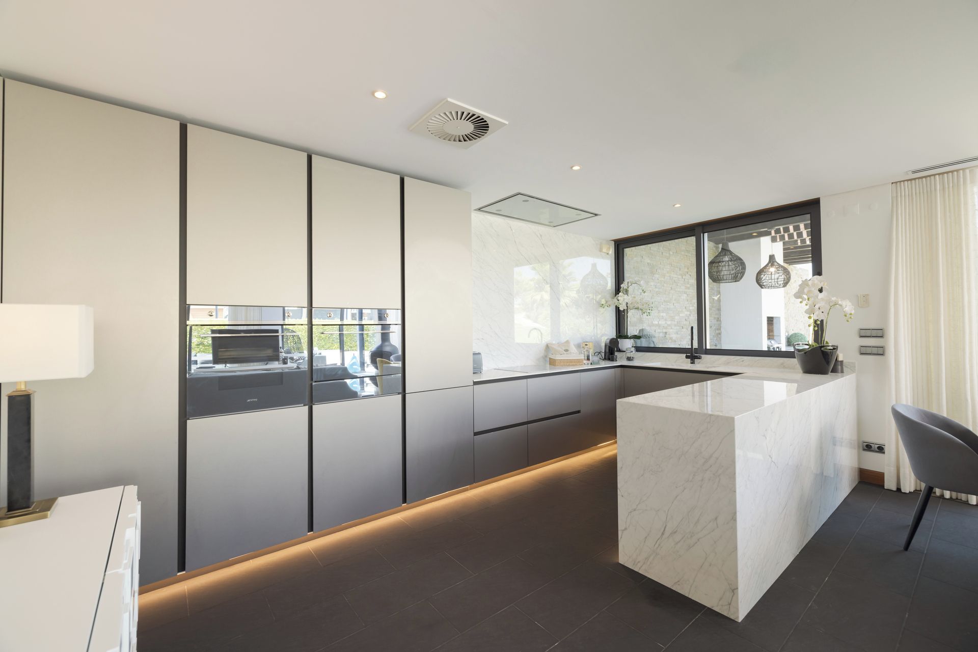 Una cocina moderna con una isla grande, piso oscuro y vistas al exterior.