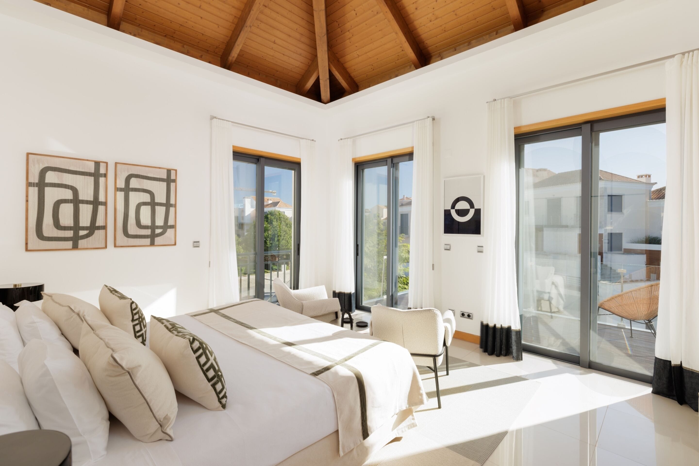 A modern hotel room with a large bed, two windows, a balcony, and a view of the outside.