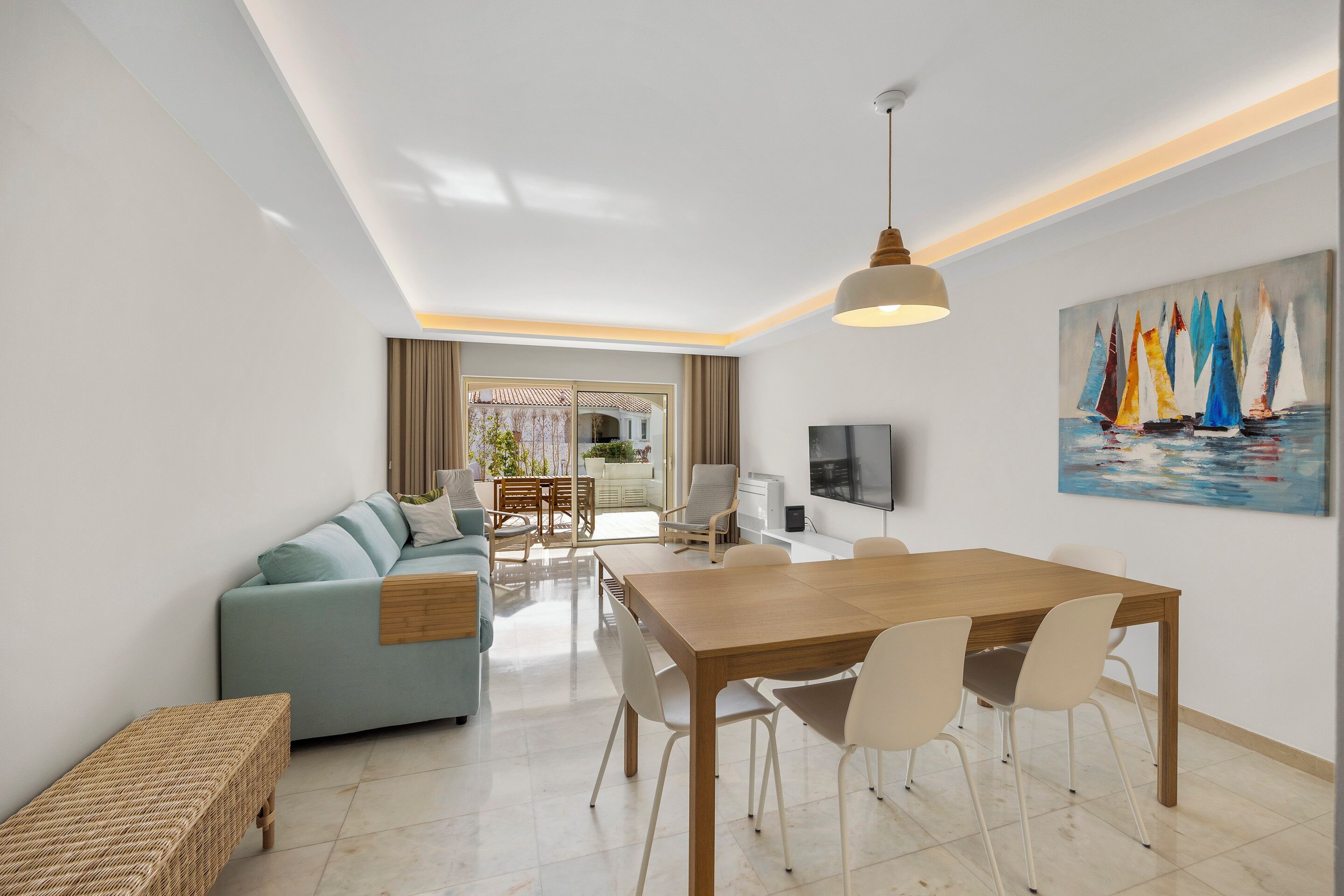 A modern living room with a sofa, dining table, chairs, and a TV.