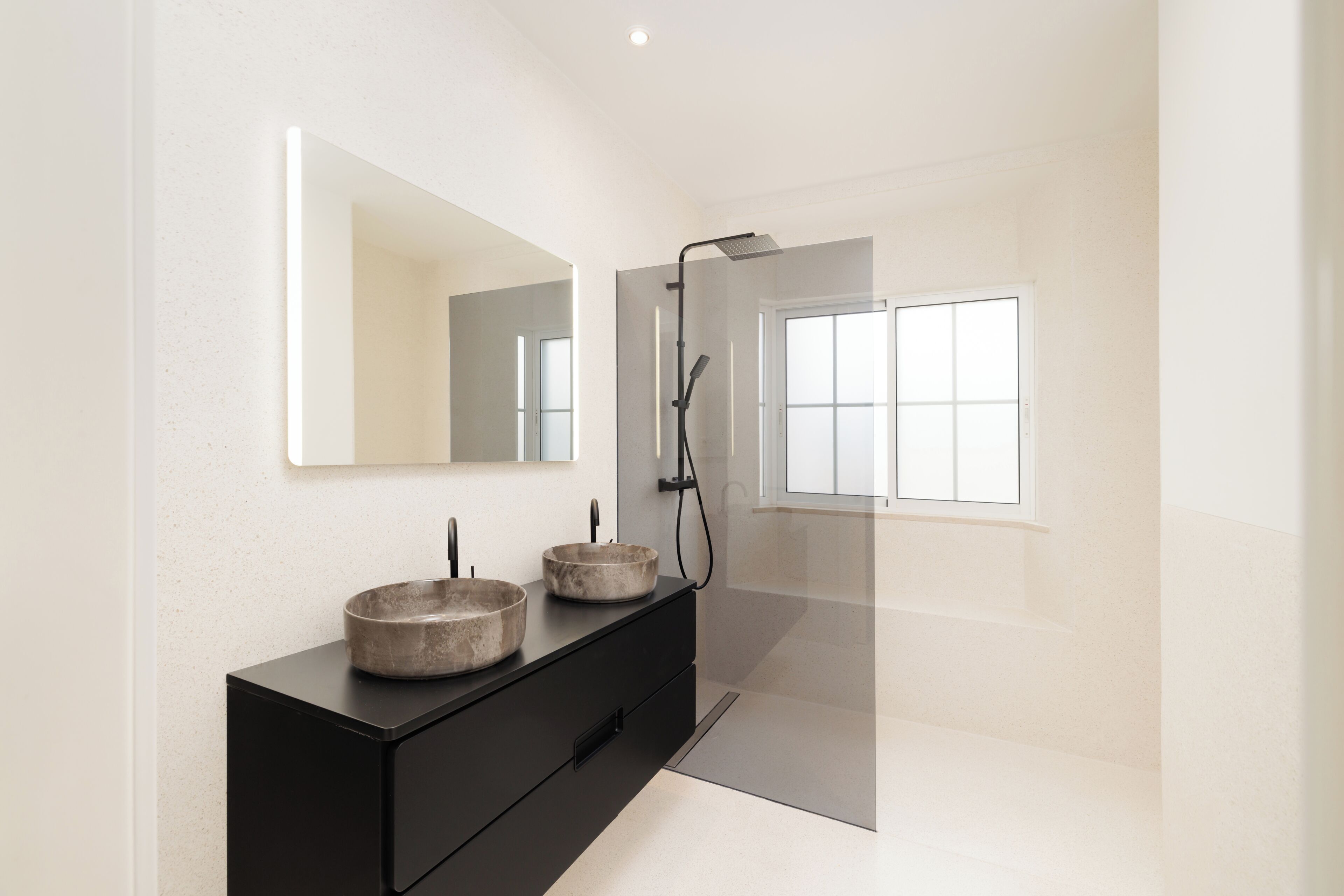 Ein modernes Badezimmer mit einem schwarzen Waschtisch, zwei runden Waschbecken, einem großen Spiegel und einer Duschkabine aus Glas.