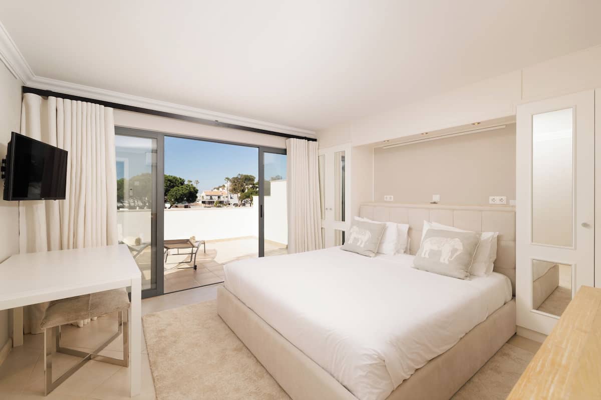 A hotel room with a large bed, a desk, a TV, and a sliding glass door to the balcony.