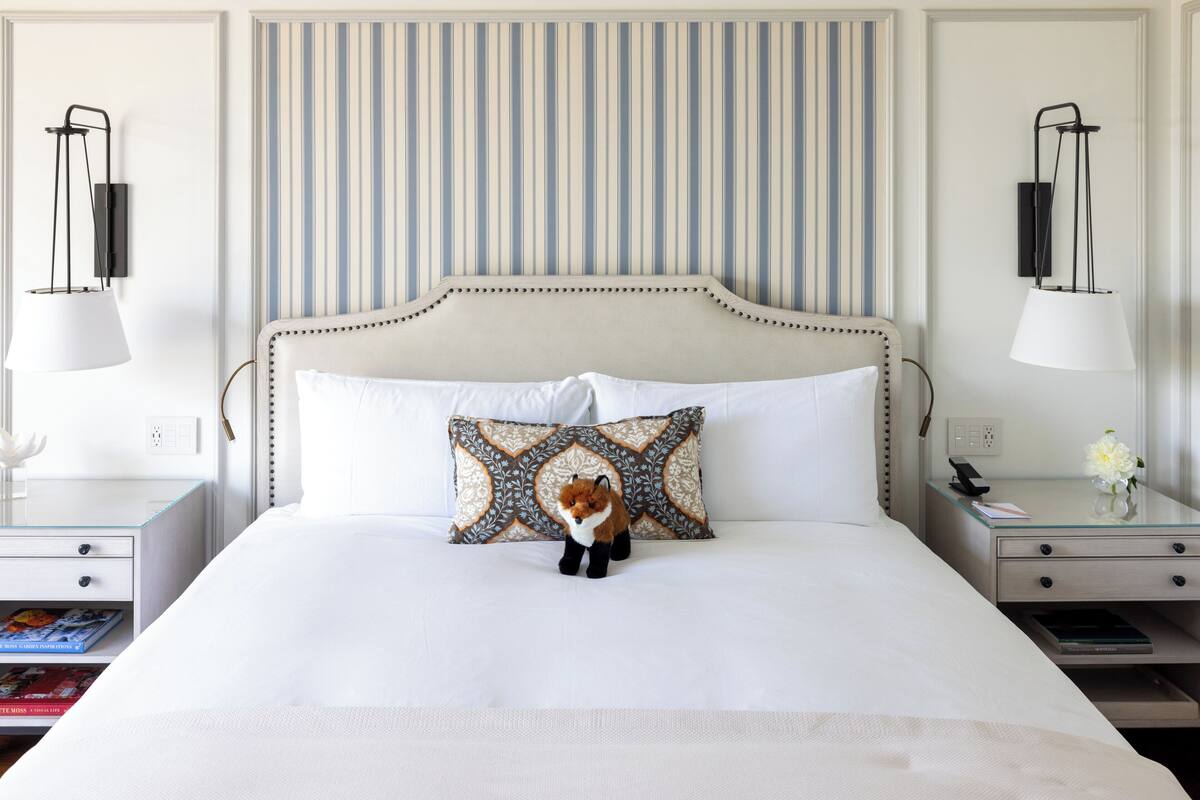 A neatly made bed with a decorative pillow, a bedside table with a lamp, and a wall with vertical stripes.