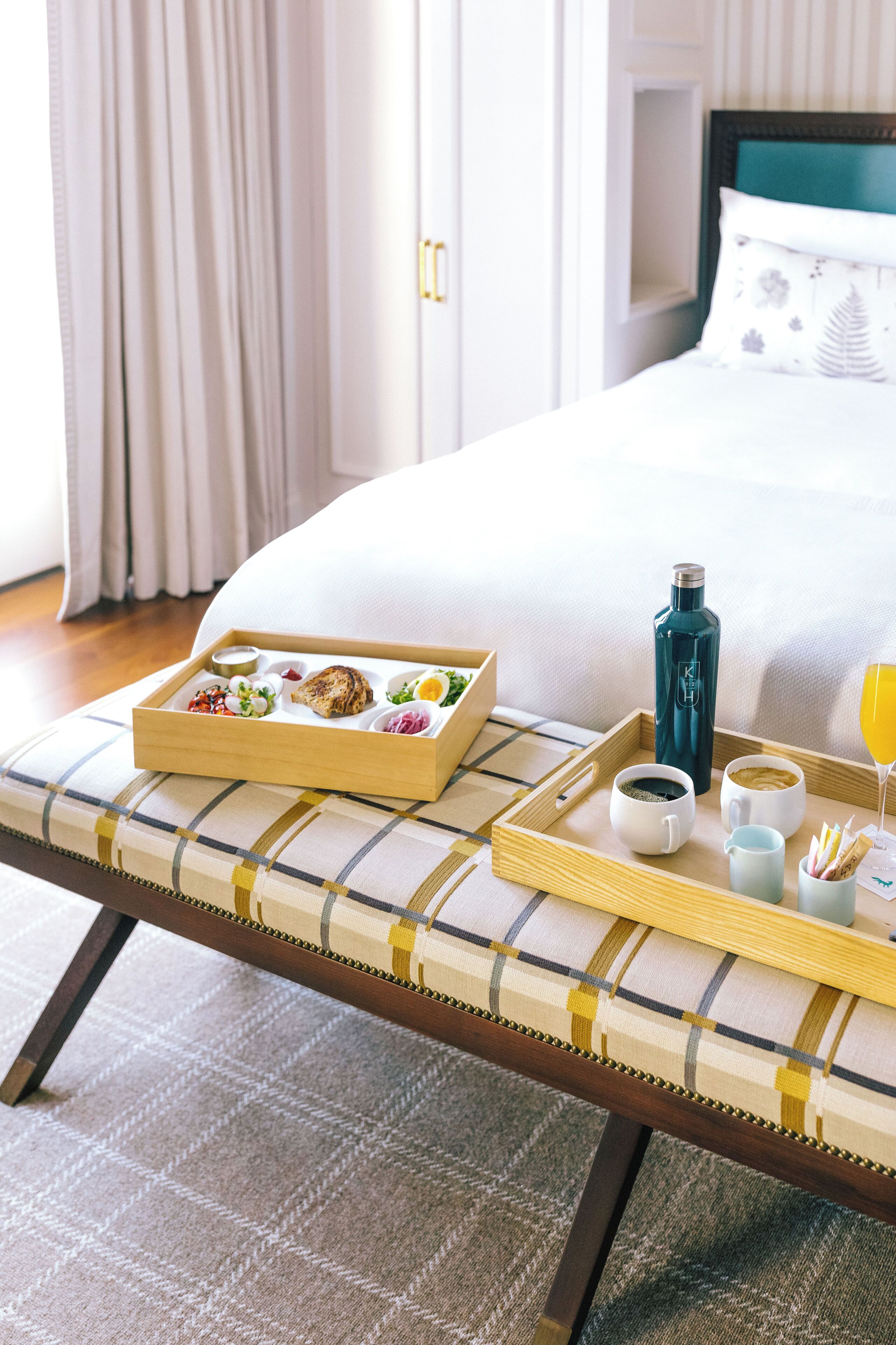 A neatly arranged breakfast tray on a bed with a pillow, a bottle, and a glass of orange juice.