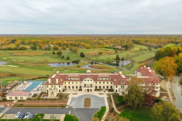 A large, historic building with a central courtyard, surrounded by a golf course and a lake.