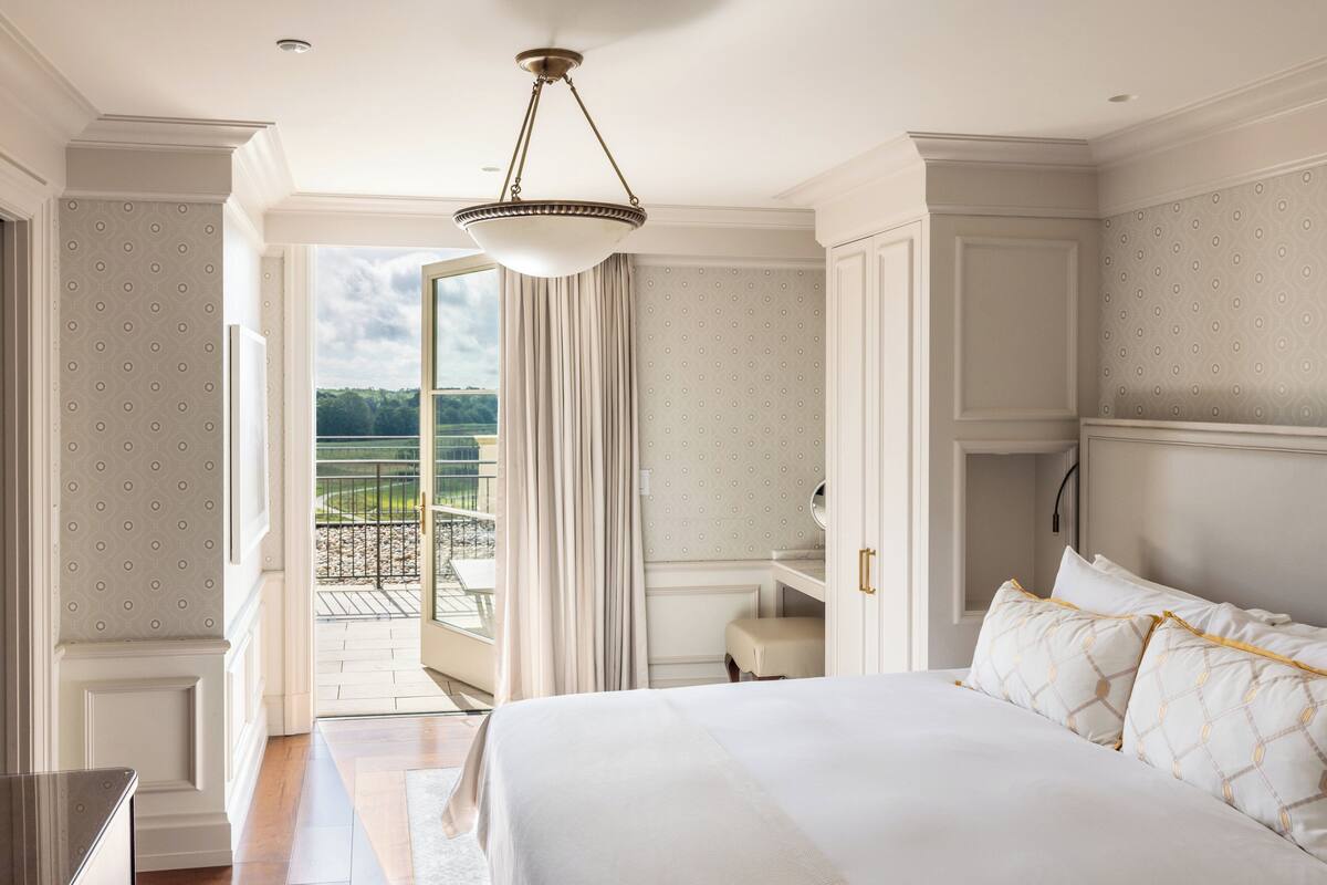 A spacious bedroom with a large bed, a walk-in closet, and a balcony with a view.