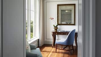 Una habitación con un escritorio de madera, una silla azul, un florero con flores y un cuadro en la pared.