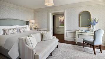 A hotel room with a large bed, a sitting area with a sofa, a desk with a chair, and a mirror on the wall.