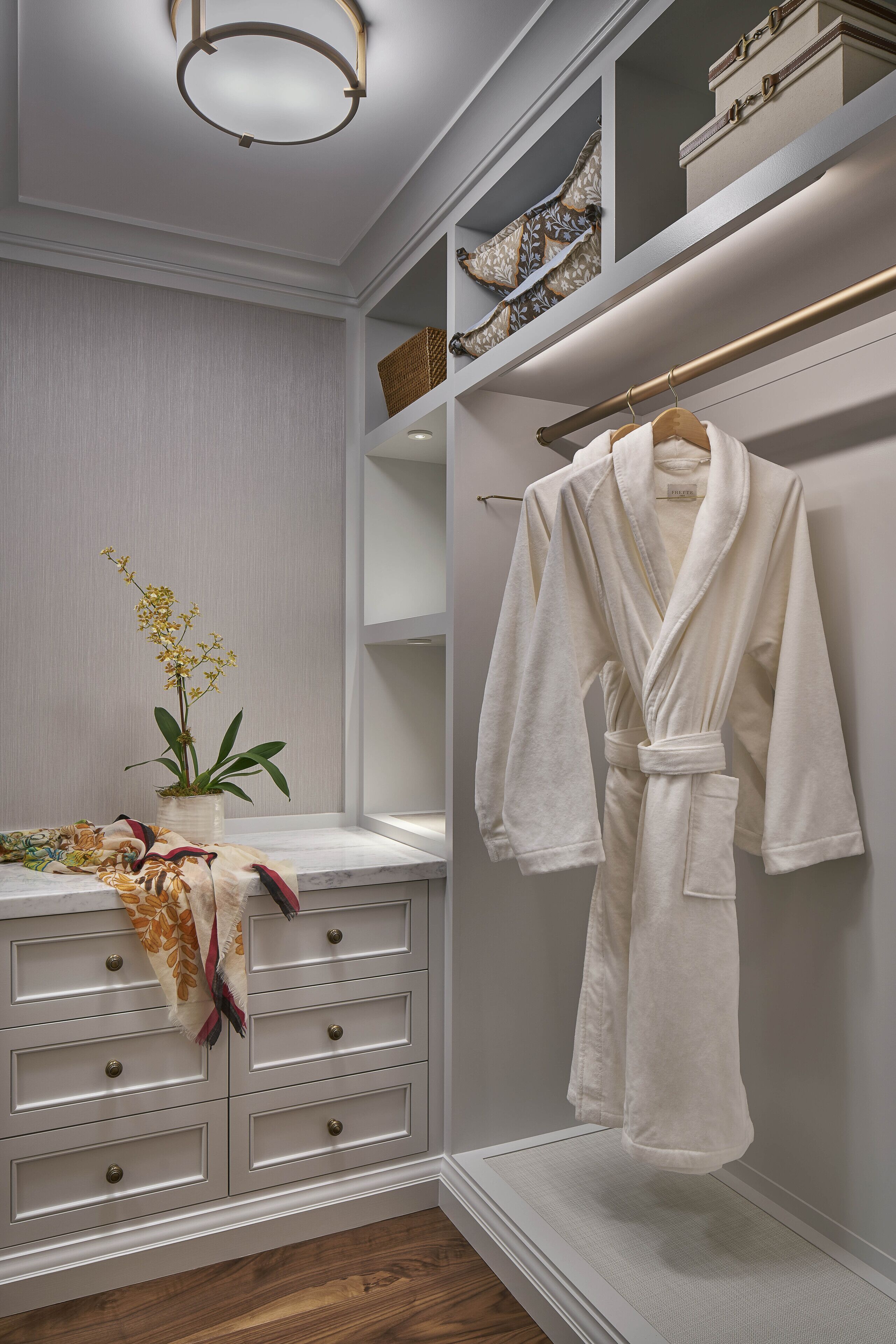 A walk-in closet with a robe hanging on a rack, a potted orchid, and a basket on the shelves.