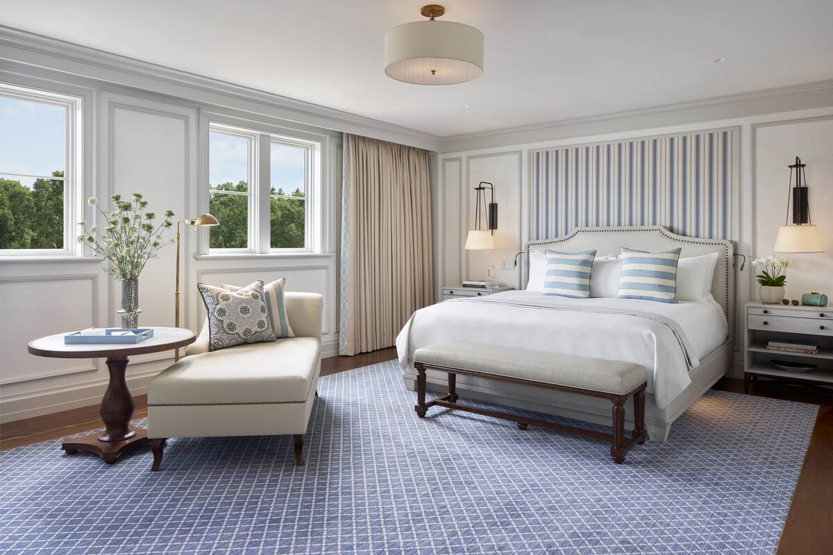 A bedroom with a large bed, a bedside table, a chair, and a window with curtains.