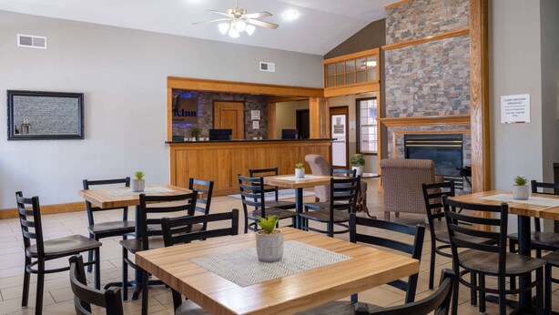 A hotel lobby with wooden tables and chairs, a reception desk, and a stone fireplace. - AmericInn by Wyndham Cedar Rapids North (Cedar Rapids)