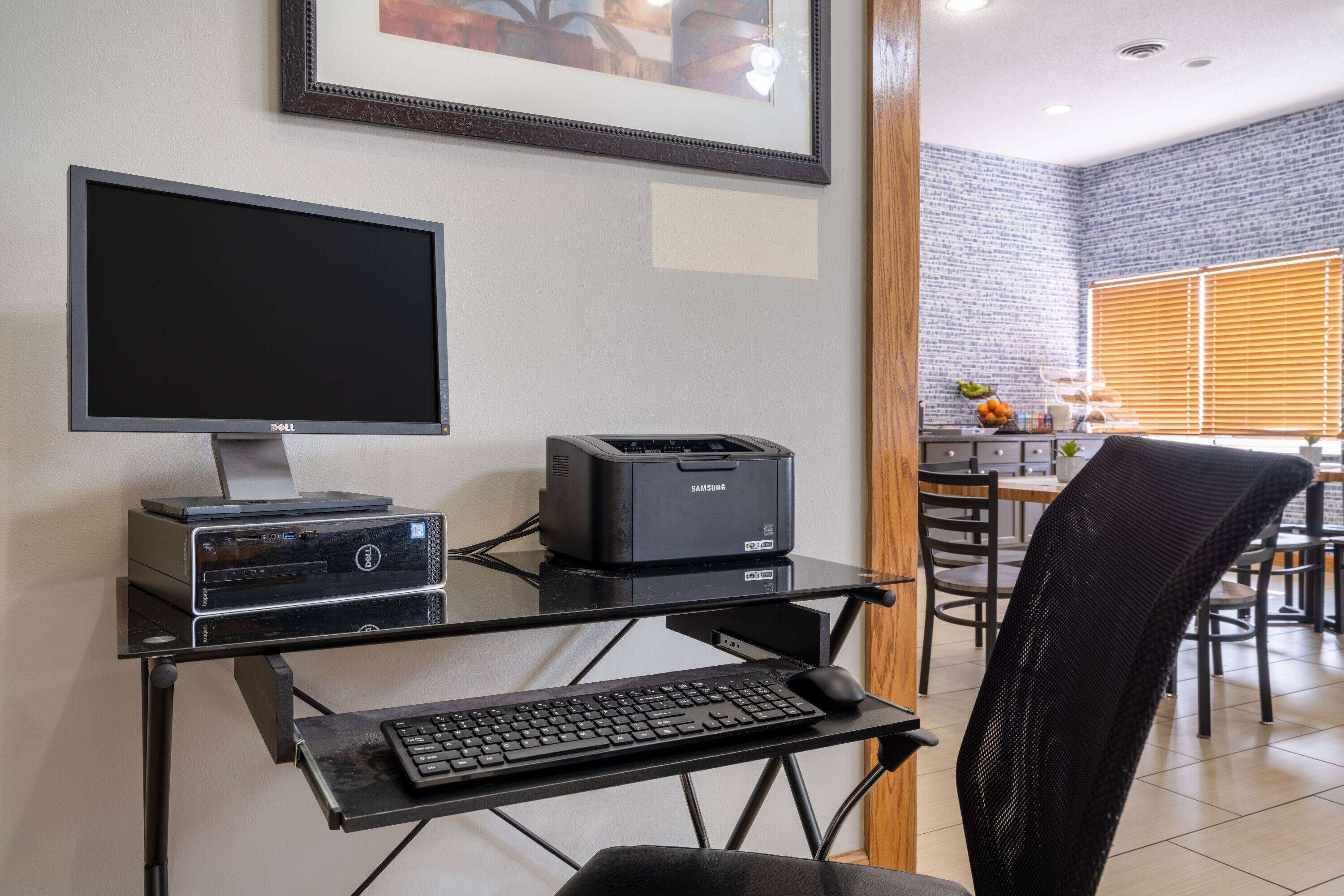 A home office setup with a desktop computer, monitor, printer, and keyboard on a glass desk.