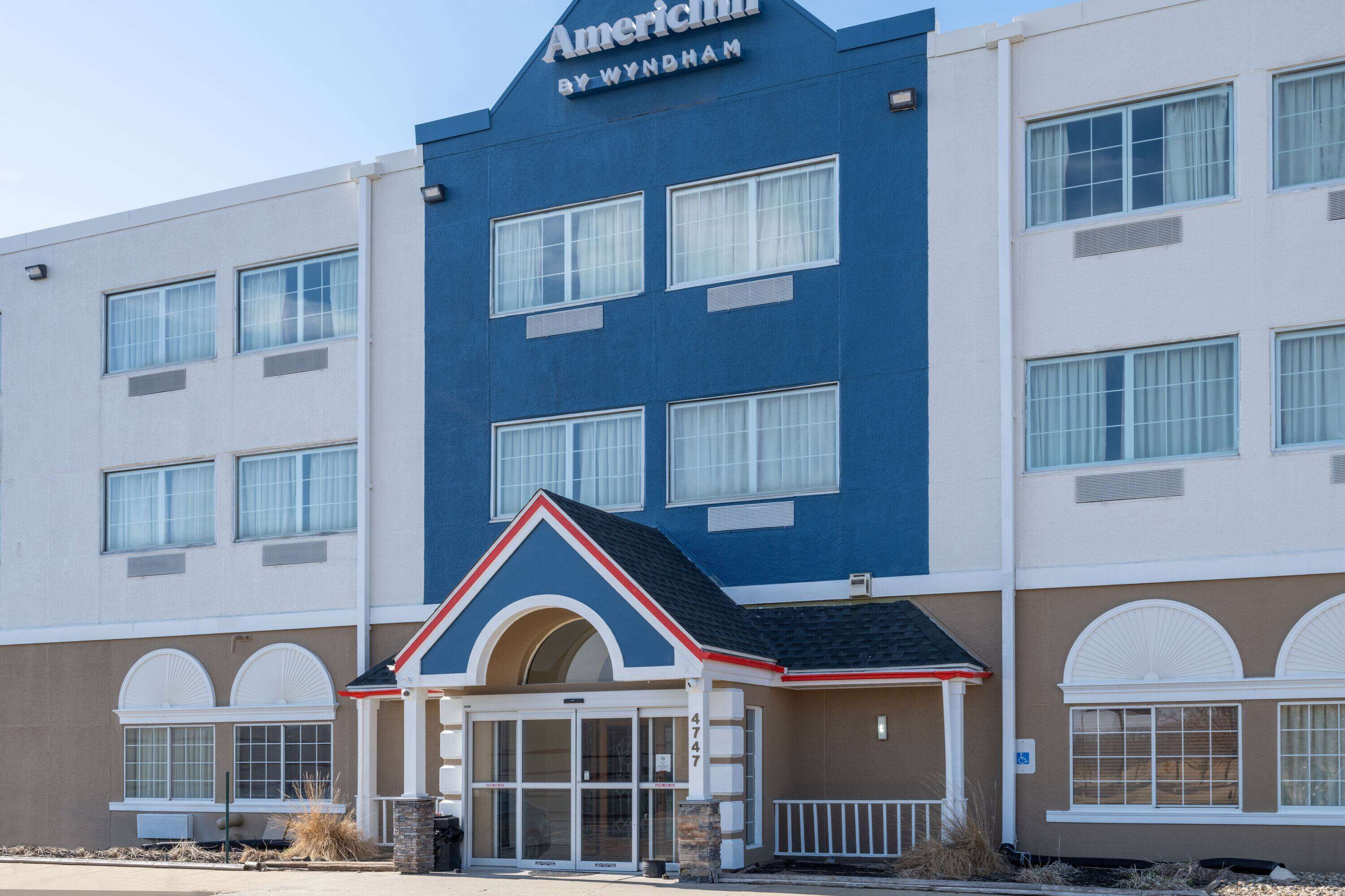 A hotel with a blue and beige facade, a central entrance with a small porch, and multiple windows.
