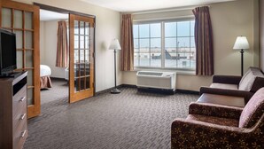 A hotel room with a large window, a sofa, a TV, a desk, and a wardrobe. - AmericInn by Wyndham Cedar Rapids North (Cedar Rapids)