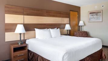 A hotel room with a large bed, two bedside tables with lamps, a wooden headboard, a brown chair, and a framed picture on the wall.