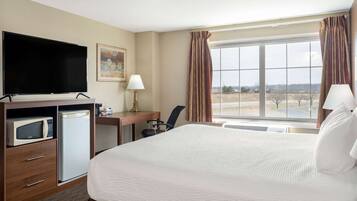 A hotel room with a bed, a desk, a television, a microwave, and a refrigerator.