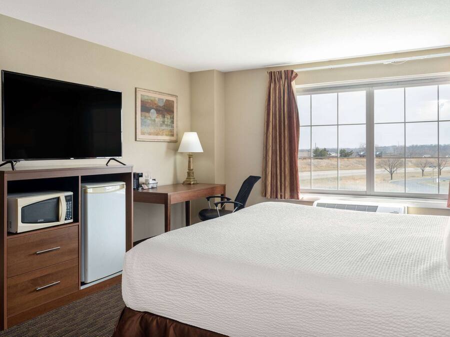 A hotel room with a bed, a desk, a television, a microwave, and a refrigerator.