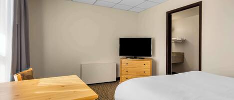 A hotel room with a bed, a wooden table, a television on a wooden dresser, and a mirror on the wall.
