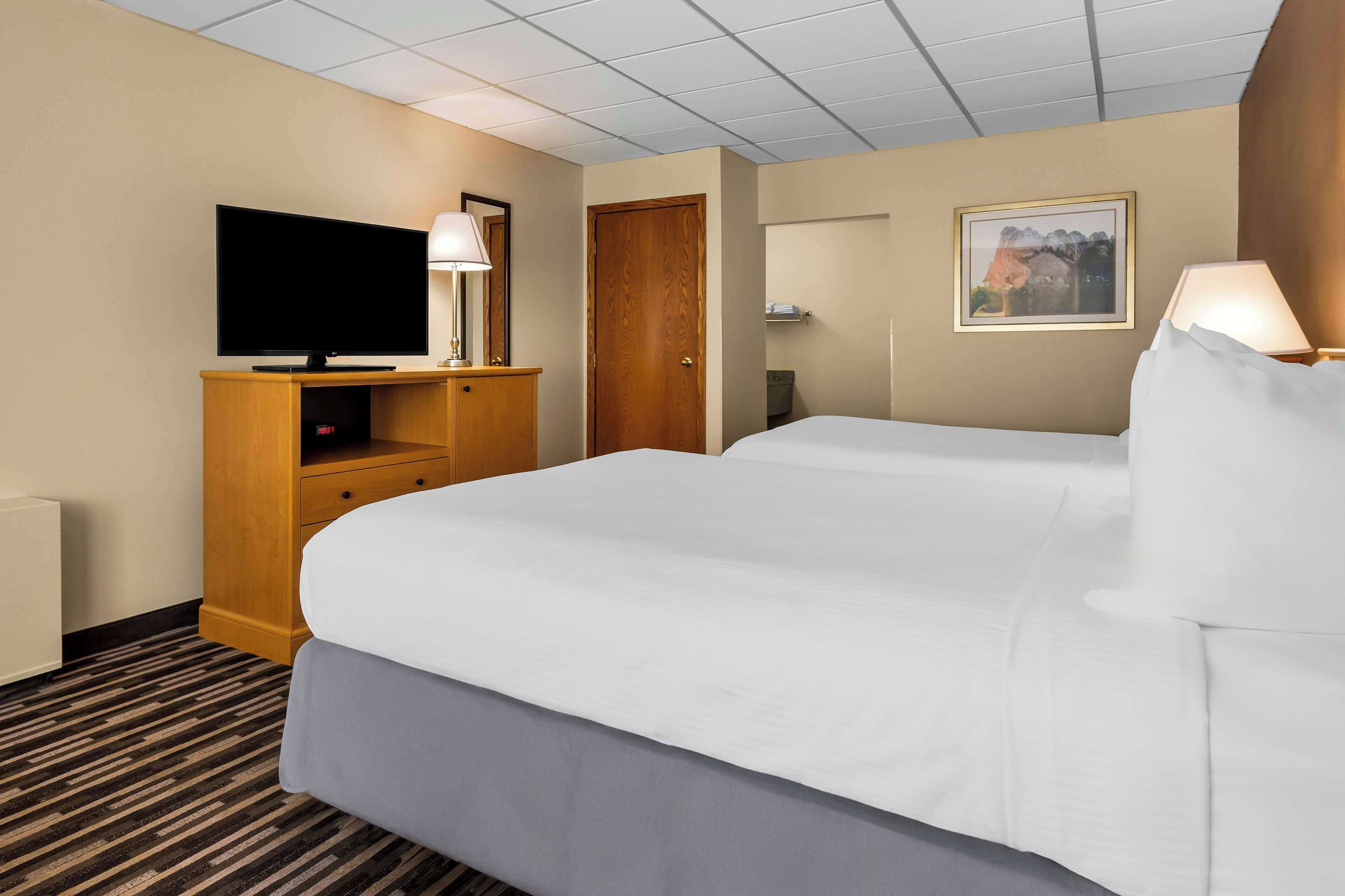 A hotel room with a large bed, a flat-screen TV, a wooden cabinet, a door, a framed picture on the wall, and a lamp.