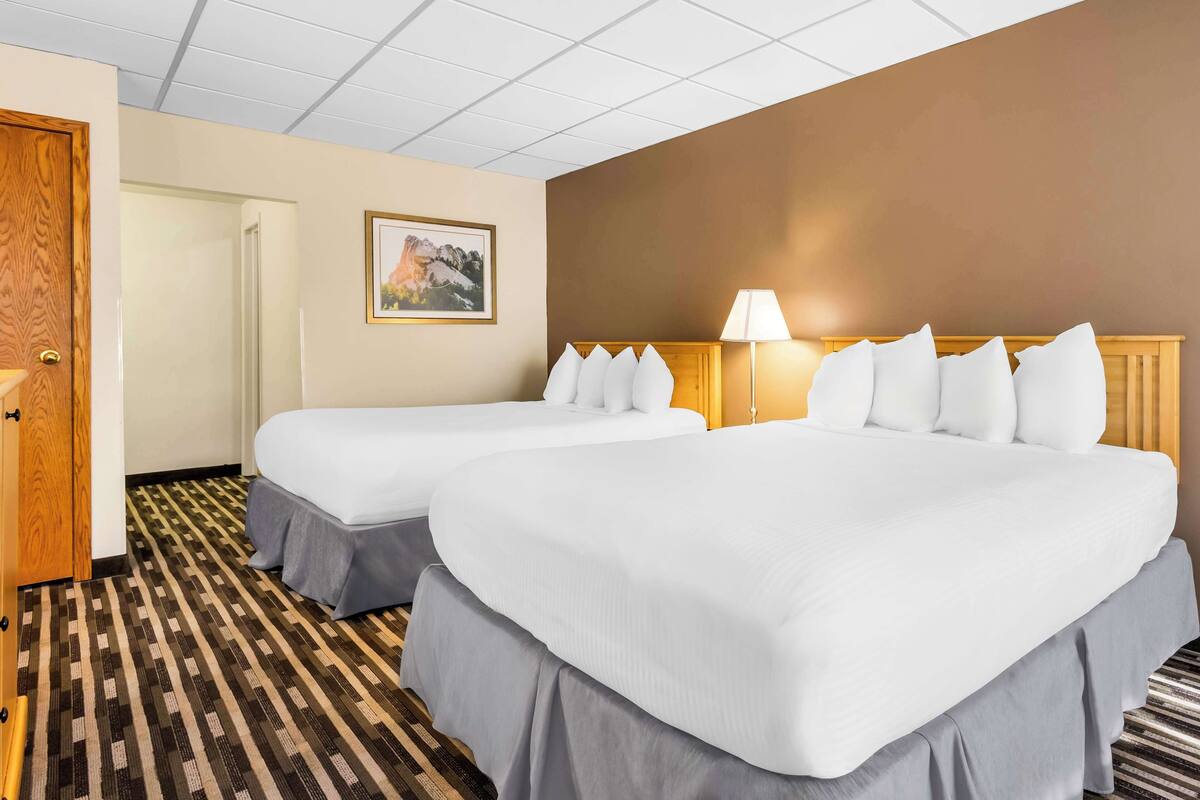 A hotel room with two beds, a wooden door, a framed picture on the wall, and a patterned carpet.