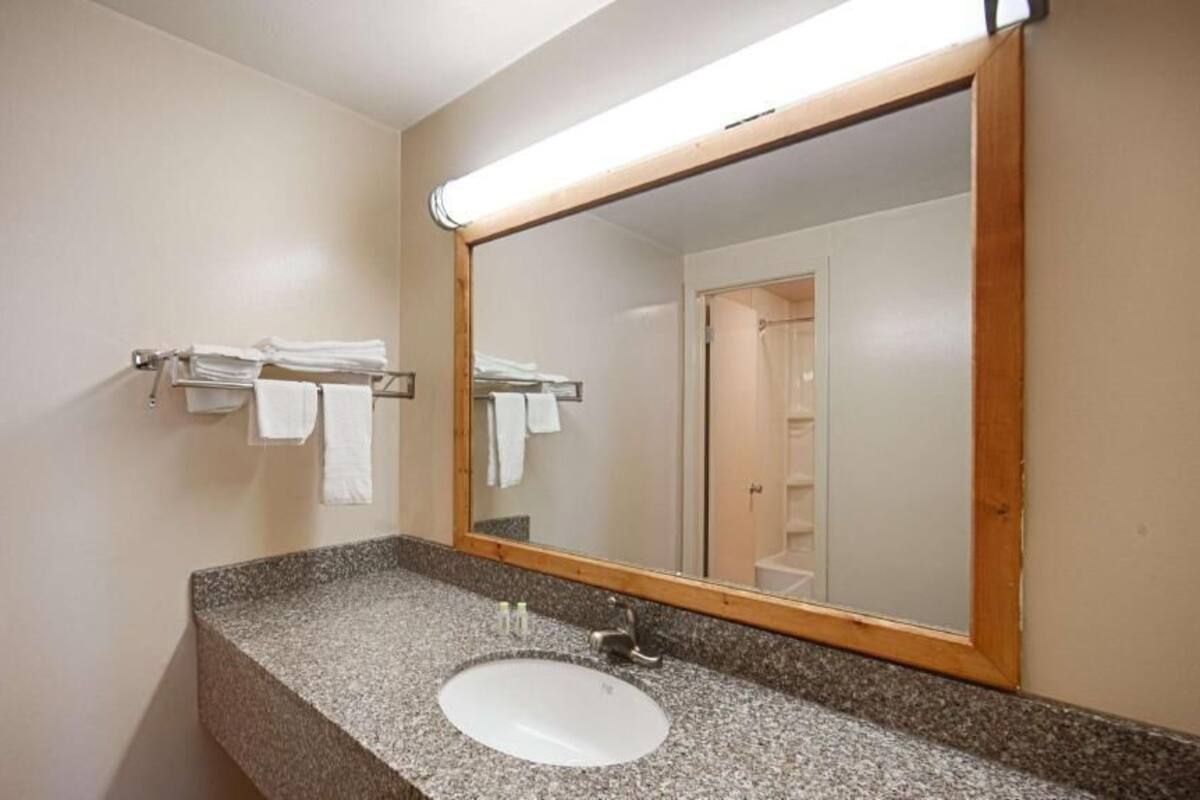 A bathroom with a granite countertop sink, a mirror with a wooden frame, and a towel rack with white towels.