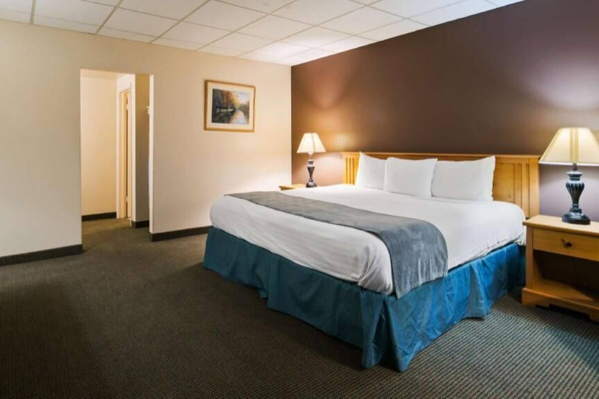 A hotel room with a bed, bedside lamps, a television, and a painting on the wall.