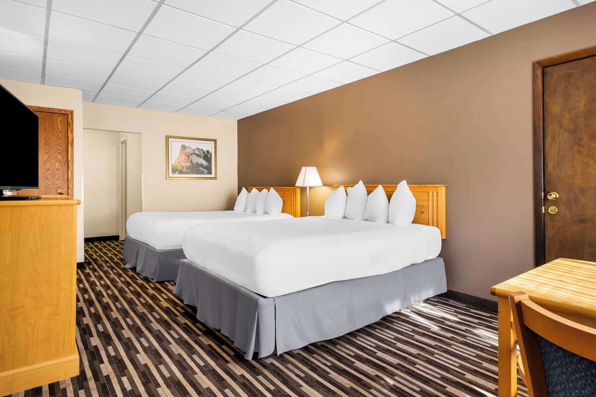 A hotel room with two beds, a desk, a TV, and a door.