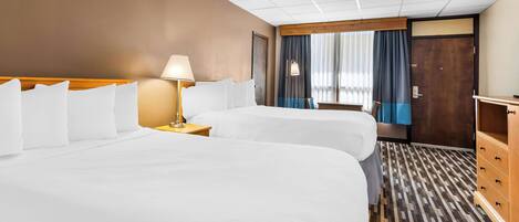 A hotel room with two beds, a wooden headboard, a nightstand with a lamp, a dresser, and a window with curtains.