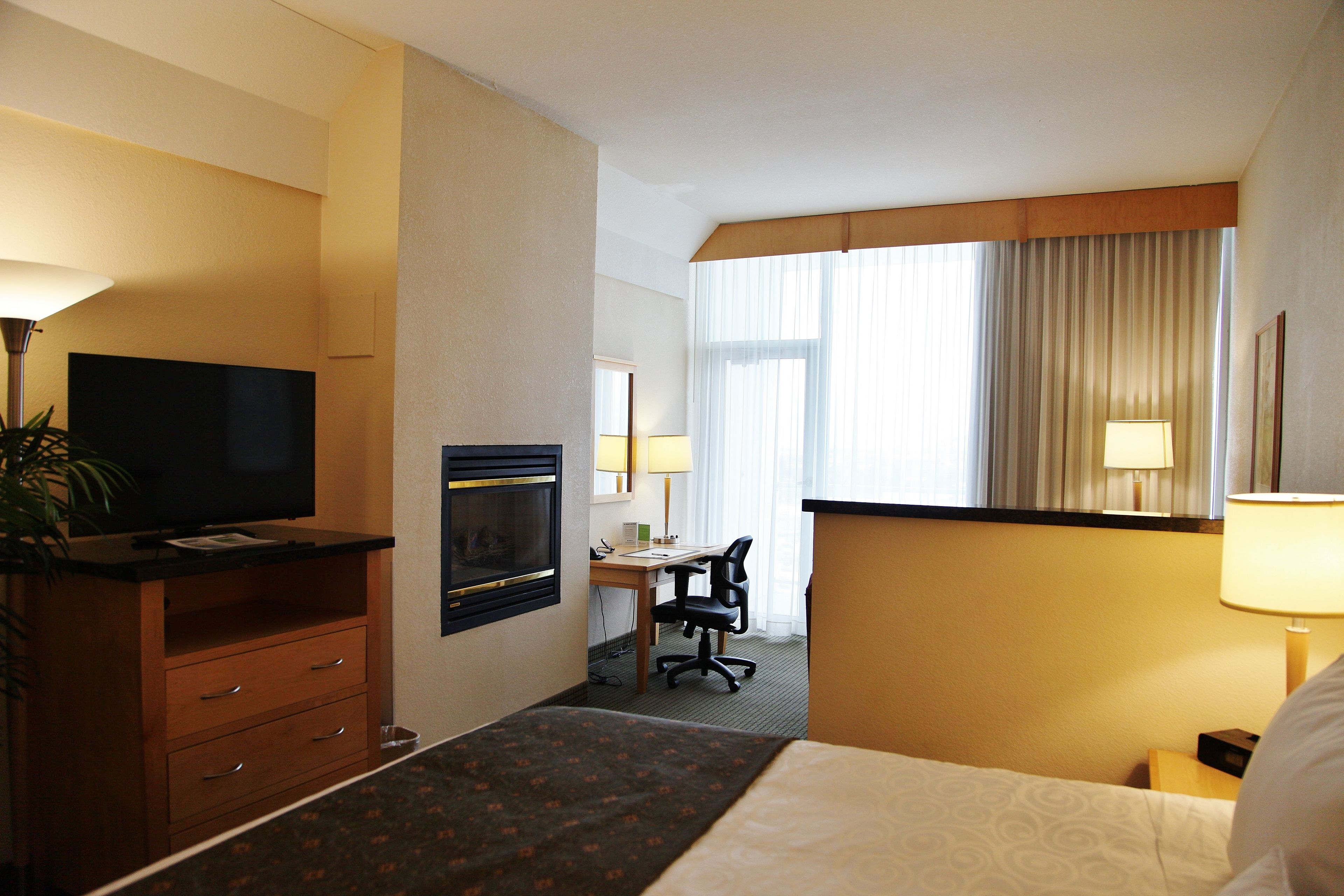 A hotel room with a bed, a desk with a chair, a television, a lamp, and a window with curtains.